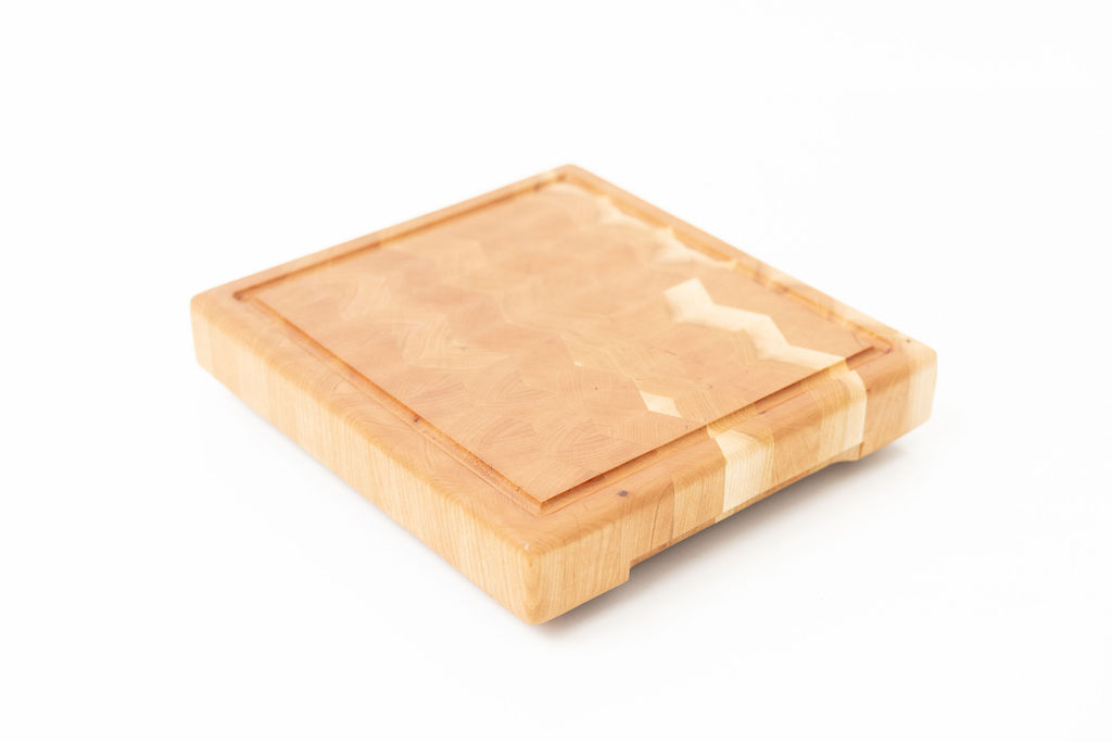 Herringbone pattern end grain cherry wood cutting board with brass feet, featuring geometric zigzag design, juice groove, and elevated profile for optimal knife preservation