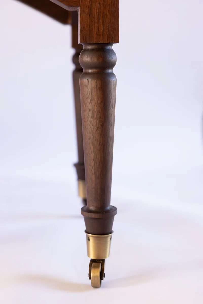 Close-up of a hand-turned walnut leg with brass caster on a custom solid walnut wood buffet — beth & co. woodworks, Sierra Vista, AZ